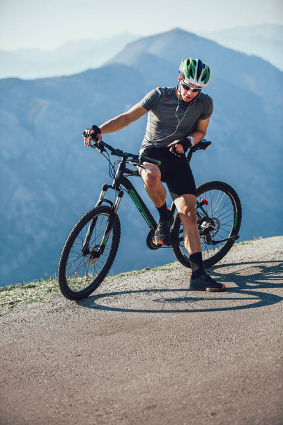 Portrait of mountain biker with helmet and sunglasses listening to music and smiling. - Photo, Image