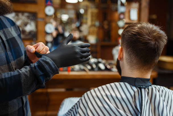 Barbeiro coloca luvas, cliente sentado na cadeira. Barbearia profissional é uma ocupação moderna. Cabeleireiro masculino e cliente no salão de cabeleireiro
 - Foto, Imagem