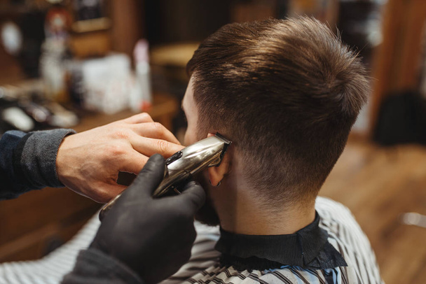 Barber holds comb and cuts the client 's hair. Professional barbershop is a trendy occupation. Male hairdresser and customer in retro style salon - Foto, afbeelding