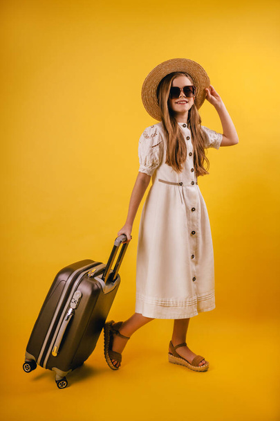 A young and young girl in a hat planned a trip abroad. Standing on a yellow background and sandals - Photo, image