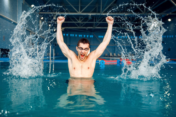 Mannelijke zwemmer in een zwembril raakt het water, de spatten rijzen op in het zwembad, bewegingszicht. Sportman aan het zwembad in het water - Foto, afbeelding