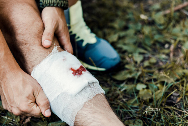 A young guy, a tourist, with a bandage bandages the injury on his leg on the way to the camp - Valokuva, kuva