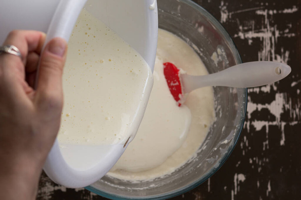 Top view of woman hand pouring whisked eggs into swollen semolina batter as ingredient for baking mannik caressole on brown background - Foto, Bild