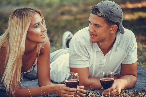 Šťastný mladý pár mluví a těší sklenku vína na romantický piknik v parku - Fotografie, Obrázek