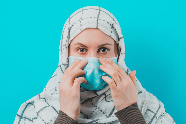 Woman in white scarf and puts mask on face on blue background.2020 - Photo, Image