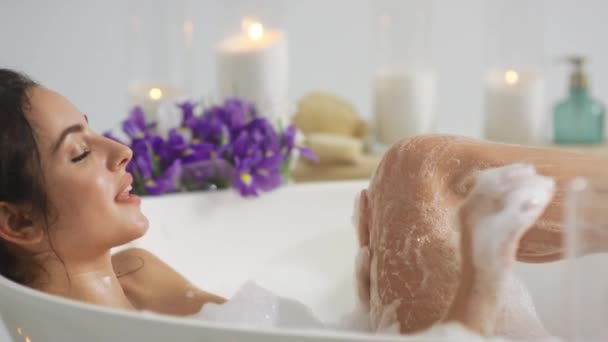 Seitenansicht der heißen Frau, die sich die Beine mit Schaum wäscht. Romantisches Mädchen badet zu Hause - Filmmaterial, Video