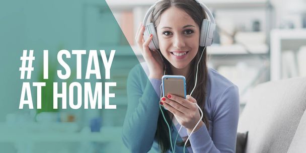 Woman listening to music with her smartphone and smiling: I stay at home social media campaign for coronavirus prevention - Photo, Image