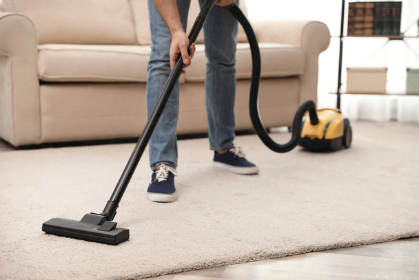 Young man using vacuum cleaner at home, closeup - Foto, afbeelding