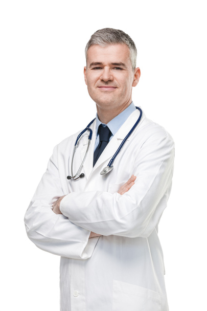 Pewny siebie lekarz w białym fartuchu laboratoryjnym i stetoskopie stojący ze złożonymi ramionami uśmiechnięty do kamery odizolowanej na biało - Zdjęcie, obraz