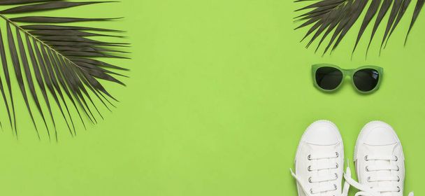 weiße Damenmode-Turnschuhe, trendige Sonnenbrille, tropische Blätter auf grünem Hintergrund. flache Lagekopierfläche von oben. Damenschuhe, Accessoires. stylische weiße Turnschuhe. Kreatives Sommerkonzept. - Foto, Bild