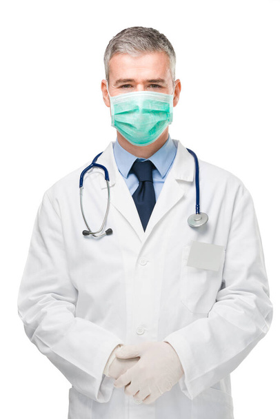 Врач носит хирургическую или респираторную маску, лабораторный халат и перчатки в качестве защиты от вируса Ковид-19 или короны в три четверти фронтальной изолированной на белом - Фото, изображение