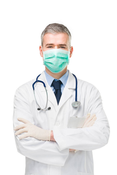 Doctor wearing a surgical or respirator mask, lab coat and gloves as protection against Covid-19 or corona virus in a three-quarter frontal isolated on white - Fotografie, Obrázek