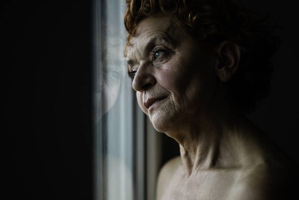 Kypsä nainen ikkunan vieressä ajattelemassa elämää
 - Valokuva, kuva