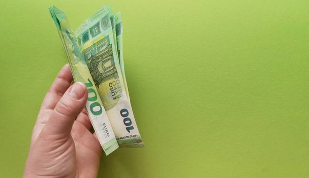 Sol elin başparmağı, 2019 yılında yeşil fonda 100 Euro tutarında basılan banknotları çeviriyor. Kâr kavramı. Avrupa para birikimi. Para kazanmak için motivasyon. - Fotoğraf, Görsel