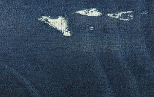 Dark indigo blue gewassen katoen jeans denim textuur achtergrond met gat en draden, close-up - Foto, afbeelding