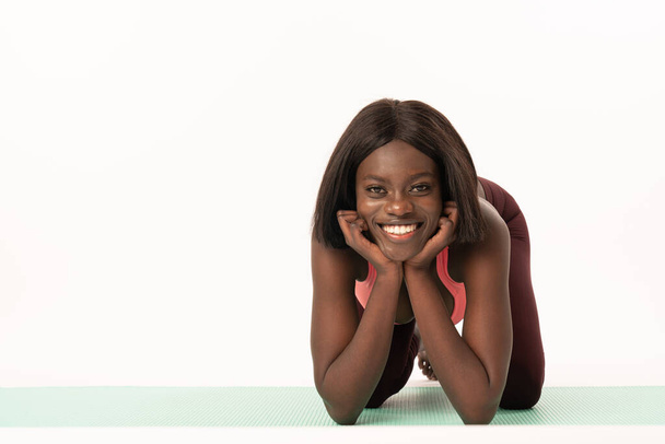 Sporty smiling african female lies on the yoga mat and looking at the camera, healthy lifestyle concept, isolated over white background - Photo, image