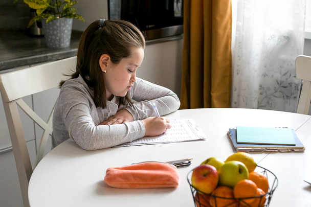 Красивая симпатичная школьница 7-8 лет, учится дома. Домашняя школа, онлайн-образование, домашнее образование, карантин, концепция коронавируса
 - Фото, изображение