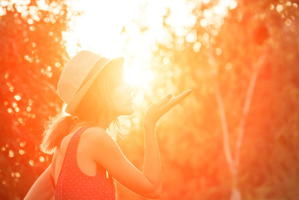 Γυναίκα φυσώντας φιλί και κρατώντας τον ήλιο σε αναγκαστική προοπτική. - Φωτογραφία, εικόνα