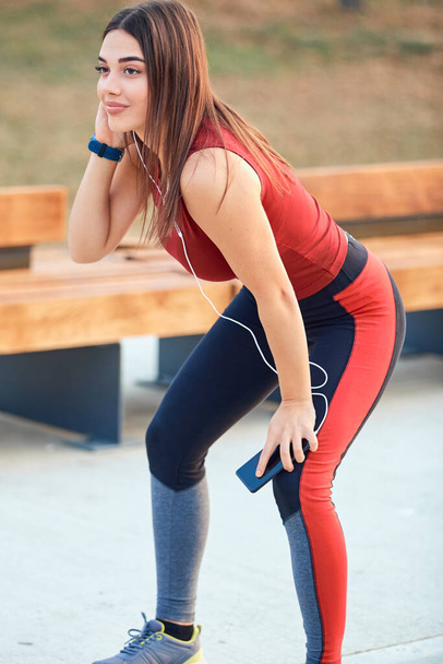 ジョギング/運動中に一時停止する携帯電話を持つ現代の若い女性. - 写真・画像