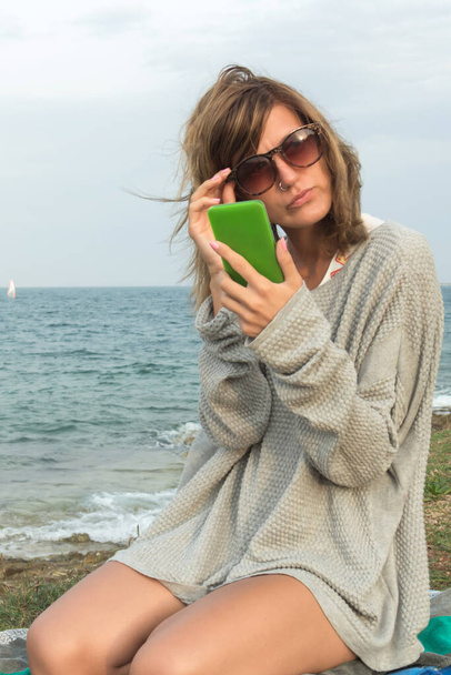 Młoda kobieta za pomocą telefonów komórkowych na plaży. - Zdjęcie, obraz