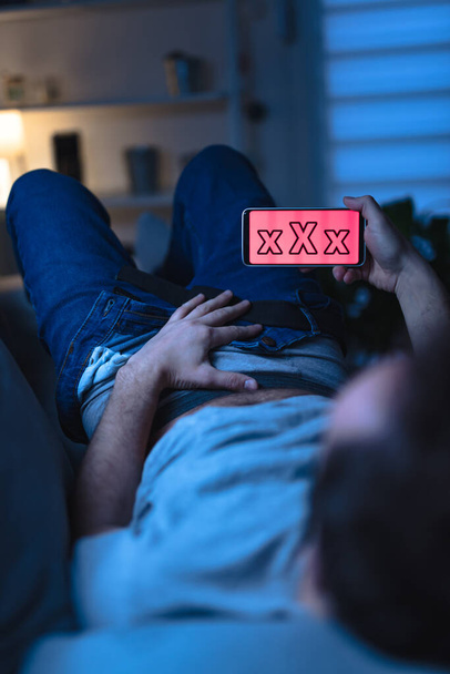 Man holding modern smartphone / cellphone and watching XX videos on a home couch. Taboo still in modern times. - Photo, Image