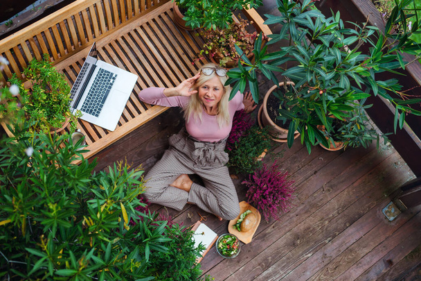 Vue du dessus de la femme âgée avec ordinateur portable assis à l'extérieur sur la terrasse, se reposant
. - Photo, image