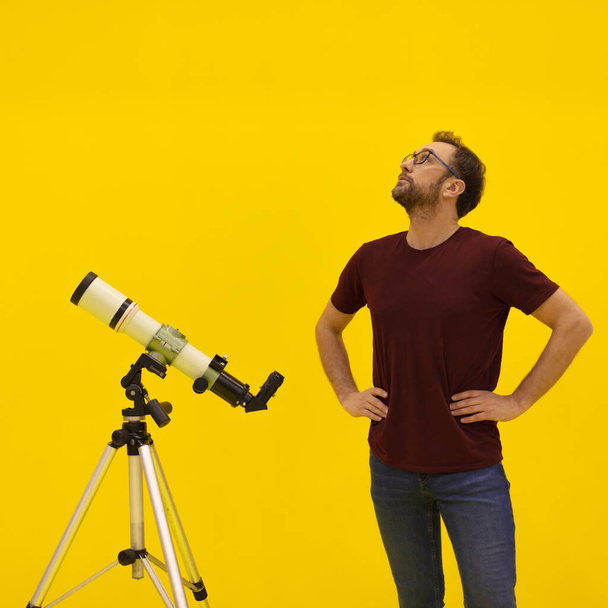 Ερασιτέχνης αστρονόμος κοιτάζει τ 'αστέρια με τηλεσκόπιο. Αστρονομία και αστρολογία έννοια. Στούντιο πλάνο σε κίτρινο φόντο. - Φωτογραφία, εικόνα