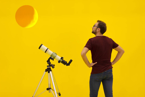 Amatör astronom teleskopla yıldızlara bakıyor. Astronomi ve astroloji konsepti. Sarı arka planda stüdyo çekimi. - Fotoğraf, Görsel