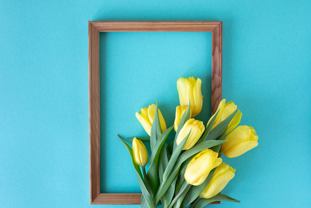 Beautiful flower arrangement. Yellow flowers tulips, empty frame for text on a blue background. Wedding. Birthday Valentine's Day. Mothers Day. Flat lay, top view - Photo, image