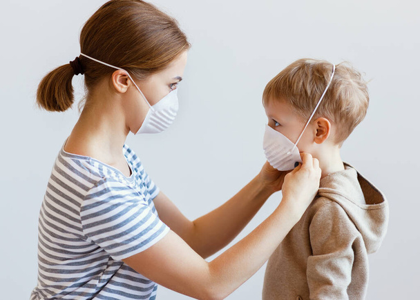 Πλευρική άποψη της ενήλικης γυναίκας που φοράει ιατρική μάσκα σε μικρό αγόρι κατά τη διάρκεια της επιδημίας coronavirus κατά γκρίζο backgroun - Φωτογραφία, εικόνα