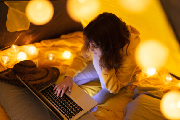 Pequena menina de 11 anos usando laptop sob sua barraca caseira dentro da sala de estar
. - Foto, Imagem