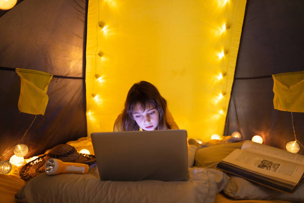 Pequena menina de 11 anos usando laptop sob sua barraca caseira dentro da sala de estar
. - Foto, Imagem
