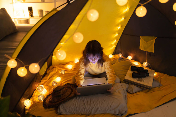 Little 11 year old girl using laptop under her home-made tent inside the living room. - Foto, Bild