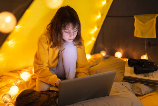 Little 11 year old girl using laptop under her home-made tent inside the living room. - Zdjęcie, obraz