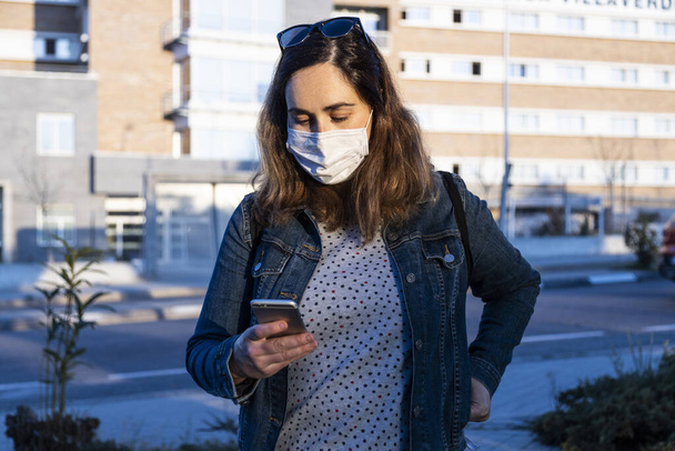 young woman chatting on her smart phone with a respirator on the street - Photo, Image