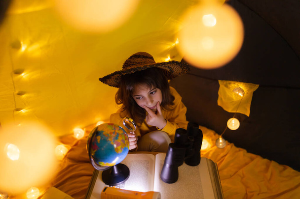 Mladá žena dítě pomocí lupy prozkoumat zeměkouli v domácí obývací pokoj stan s lehkými kuličkami. - Fotografie, Obrázek