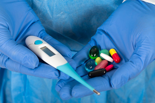Imagen de cerca del cirujano sosteniendo termómetro digital y medicamentos sobre fondo azul
 - Foto, imagen