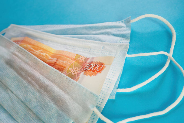 Face masks and banknote of 5000 rubles on blue background. Concept of deficit, speculation and sold out of medical masks. Selective focus - Foto, Imagem