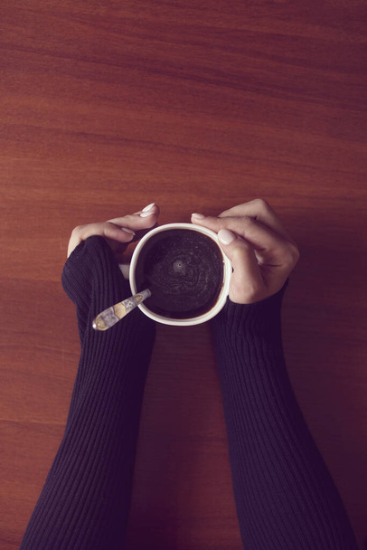 Una donna in caffetteria. Una donna irriconoscibile che beve caffè in un ambiente familiare accogliente. Mani femminili che tengono la tazza di caffè su sfondo tavolo di legno
 - Foto, immagini