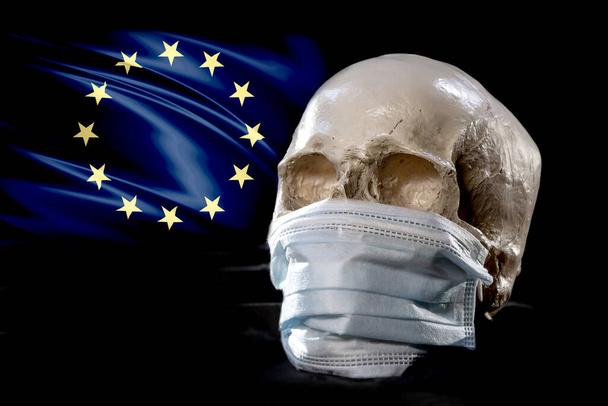 A human skull in a medical mask on the background of the European flag. Concept: mortality in Europe from coronavirus, global pandemic, infection with a deadly virus. - Foto, afbeelding
