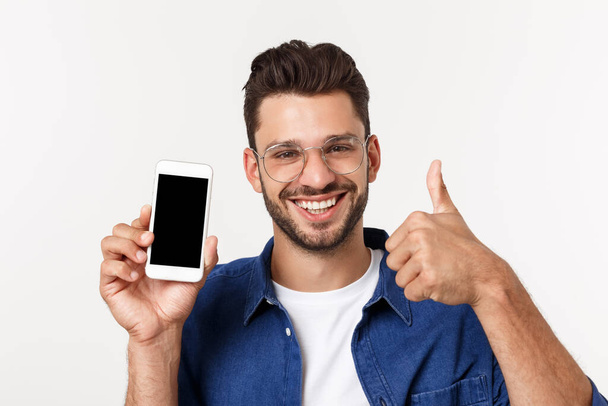 Jovem mostrando uma tela de telefone inteligente em branco com polegares isolados em um fundo branco
. - Foto, Imagem