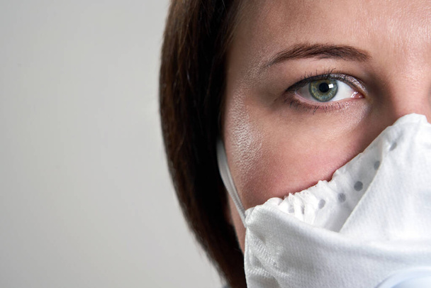 Gewassen gezicht van jonge vrouw met gezichtsmasker voor bescherming tegen corona virus over grijze achtergrond met kopieerruimte - Foto, afbeelding