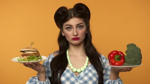 Niepewny pin up kobieta gospodarstwa burger i świeże warzywa - Materiał filmowy, wideo