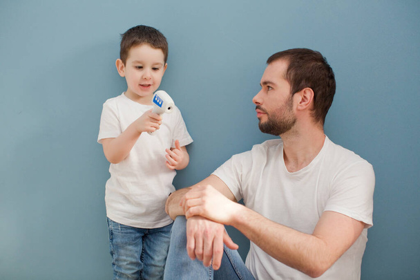 mały chłopiec i jego ojciec za pomocą termometru podczerwieni na niebieskim tle - Zdjęcie, obraz