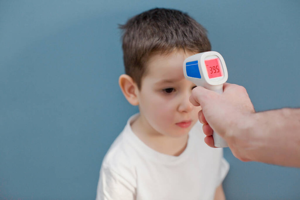 using infrared thermometer to measure child's body temperature on a blue background - Foto, afbeelding