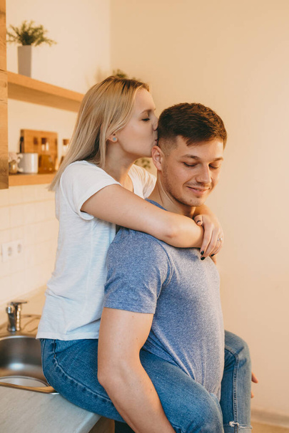 Charming blonde caucasian lady embracing her lover and kissing him in the kitchen - Fotoğraf, Görsel