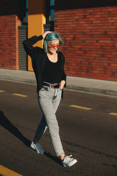 Blauhaarige Kaukasierin mit Brille läuft auf der Straße und posiert gegen die Sonne - Foto, Bild