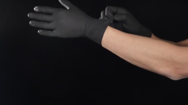 Mężczyzna lekarz zakłada czarne rękawice ochronne przed zabiegiem strzał na czarnym tle. filmik o ruchu maciory. Przenoszenie męskich rąk zakładanie egzaminów lub rękawic medycznych. Pełny hd - Materiał filmowy, wideo