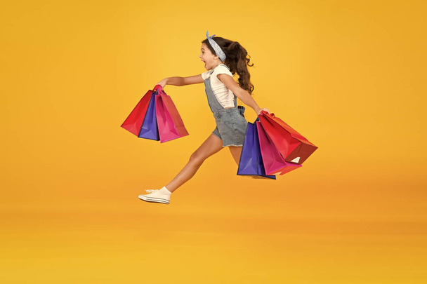 Kids fashion. Sales and discounts. happy small girl running after successful shopping. energetic child jump with heavy bags. holiday gifts in packages. cyber monday. hurry up its total sale - Foto, Bild