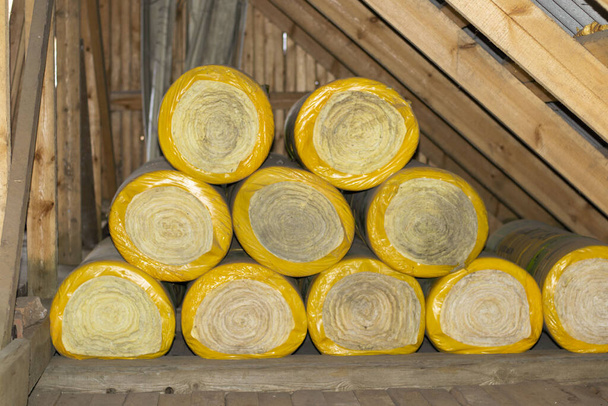 rouleaux d'isolation dans un emballage jaune dans le grenier d'une maison en bois. prêt à l'emploi, vue latérale
. - Photo, image